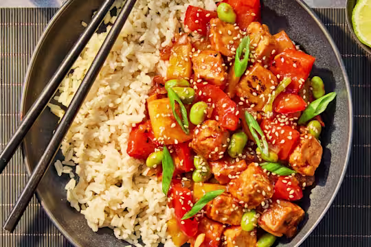 Quorn sweet and sour, served with Quorn Pieces, lime wedges on a plate with chopsticks on top.