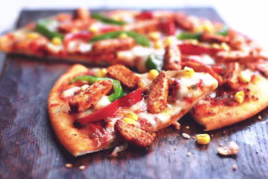 A pizza topped with cheese, red and green peppers, corn, and Quorn Pieces.