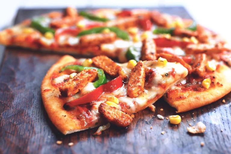 A pizza topped with cheese, red and green peppers, corn, and Quorn Pieces.