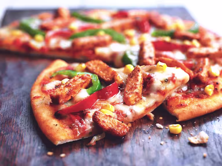 A pizza topped with cheese, red and green peppers, corn, and Quorn Pieces.