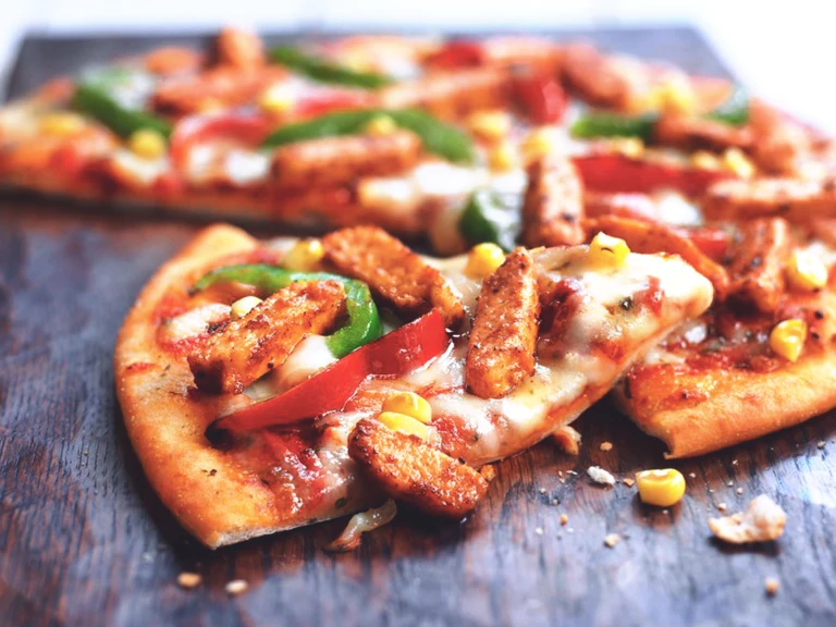 A pizza topped with cheese, red and green peppers, corn, and Quorn Pieces.