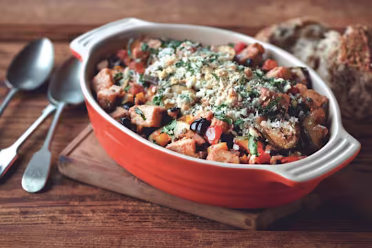 An orange baking dish filled with eggplant, zucchini, tomatoes, and Quorn Pieces topped with breadcrumbs and basil.