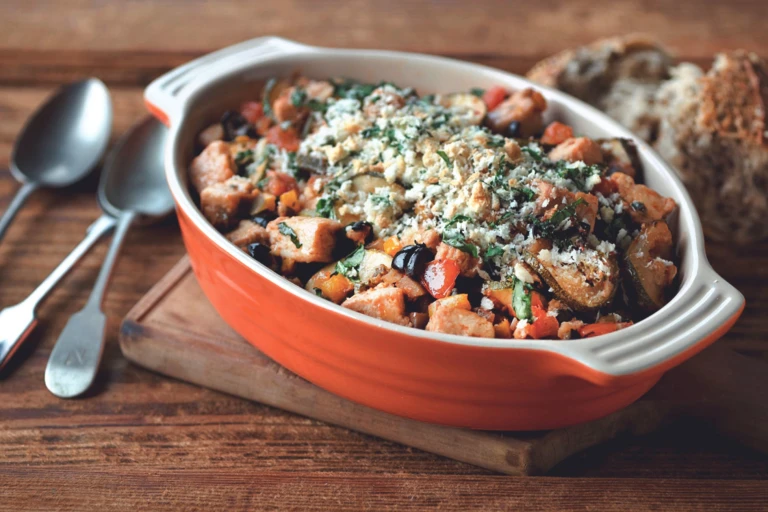 An orange baking dish filled with eggplant, zucchini, tomatoes, and Quorn Pieces topped with breadcrumbs and basil.