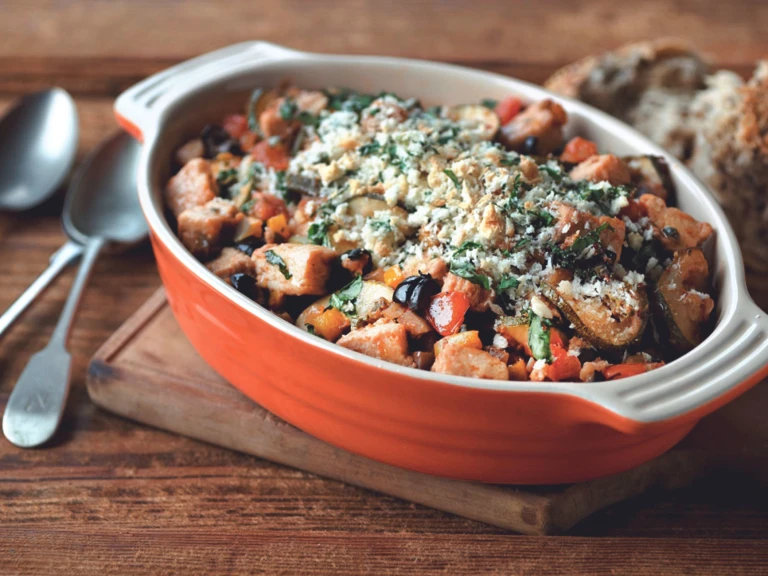 An orange baking dish filled with eggplant, zucchini, tomatoes, and Quorn Pieces topped with breadcrumbs and basil.