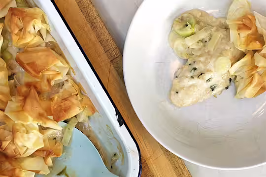 A baking tray containing filo pastry pie with a bowl filled with a serving of crispy filo pie made with Quorn Fillets.