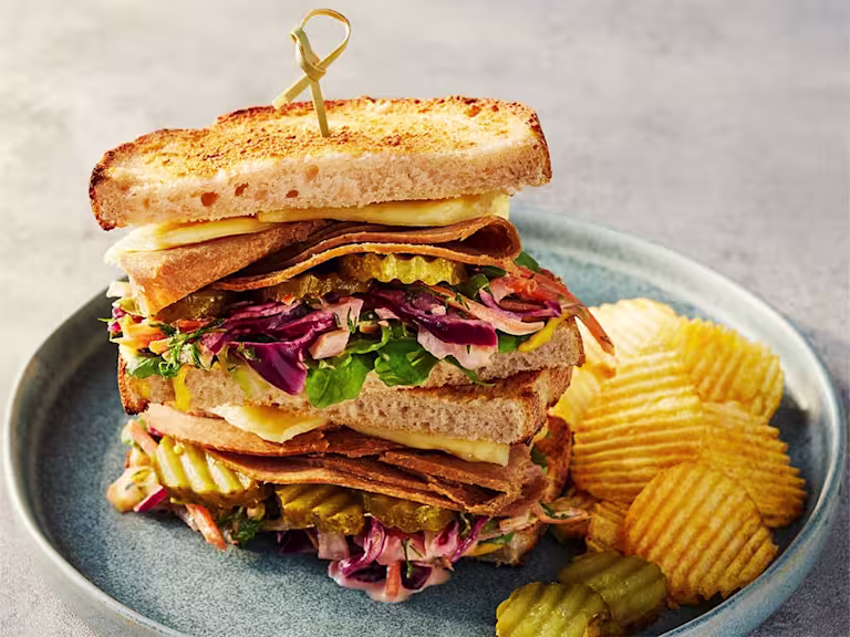 Quorn Roast Beef Vegetarian Reuben sandwich displaying the fillings with crisps on the side.