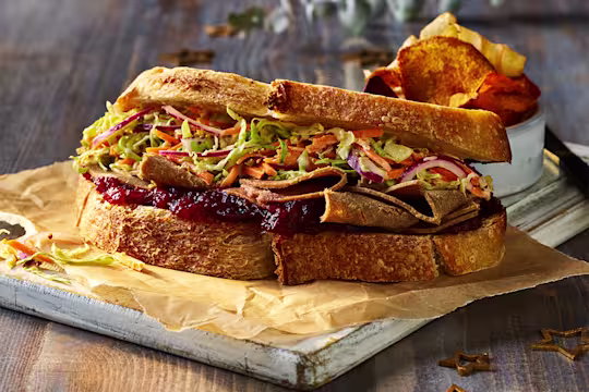 A Festive Roast Beef And Cranberry Vegan Sandwich served on a white board.