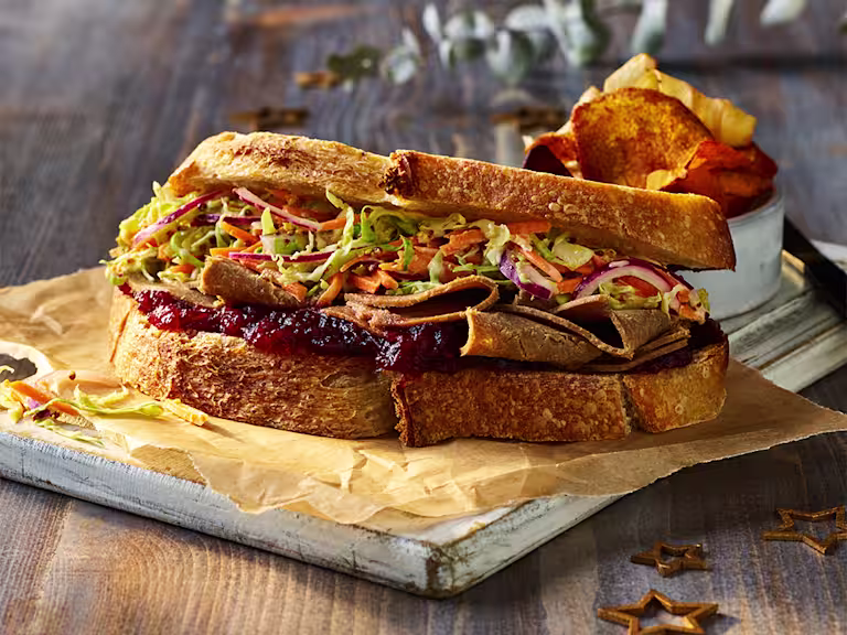 A Festive Roast Beef And Cranberry Vegan Sandwich served on a white board.