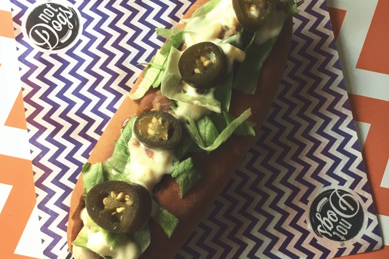 Jamaican Me Crazy Quorn Sausage hot dog topped with lettuce, mayonnaise and jalapenos served on a blue and white zig zag napkin