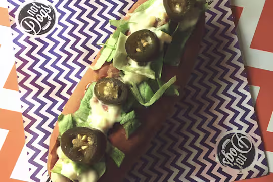 Jamaican Me Crazy Quorn Sausage hot dog topped with lettuce, mayonnaise and jalapenos served on a blue and white zig zag napkin