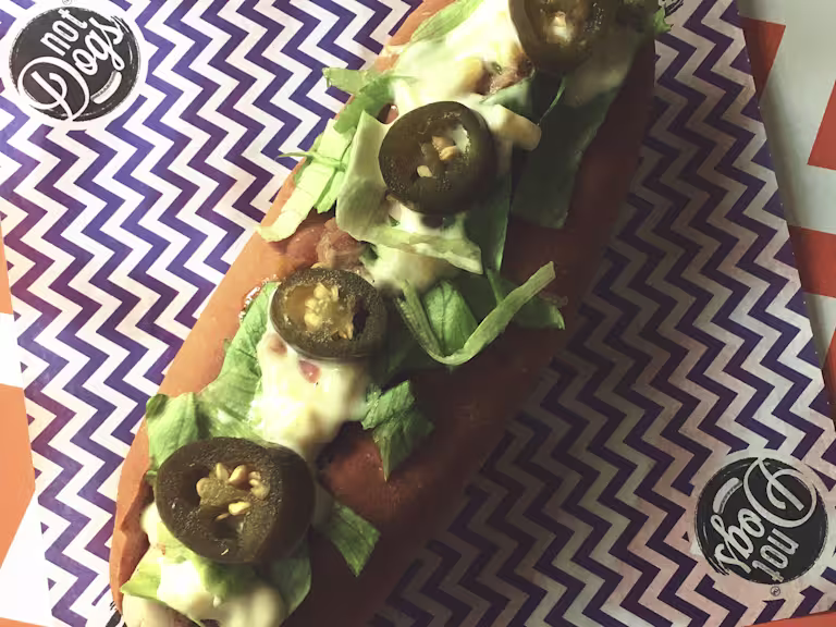 Jamaican Me Crazy Quorn Sausage hot dog topped with lettuce, mayonnaise and jalapenos served on a blue and white zig zag napkin