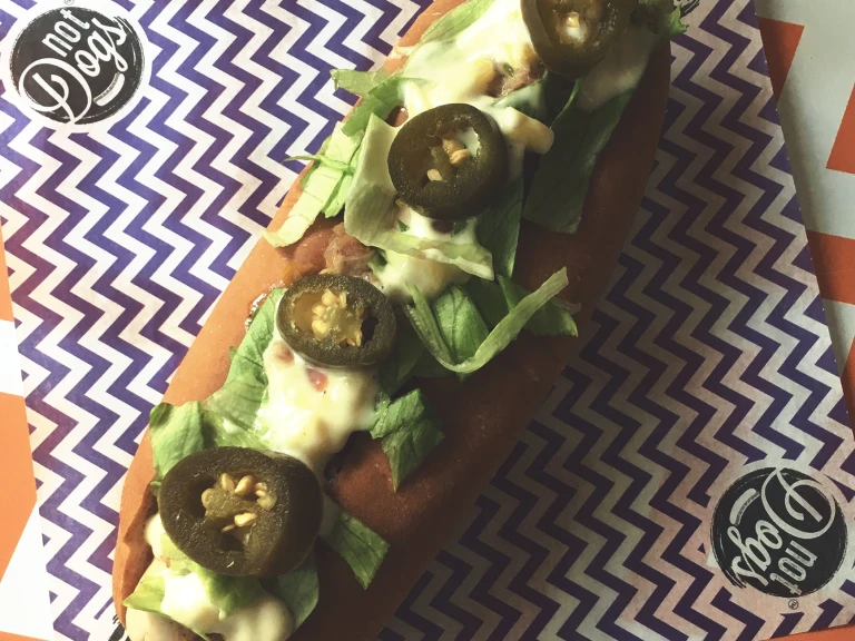 Jamaican Me Crazy Quorn Sausage hot dog topped with lettuce, mayonnaise and jalapenos served on a blue and white zig zag napkin