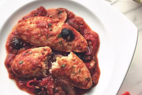 Meatless Quorn Fillets chicken cacciatore served in a dish, with one fillet half cut, garnished with olives