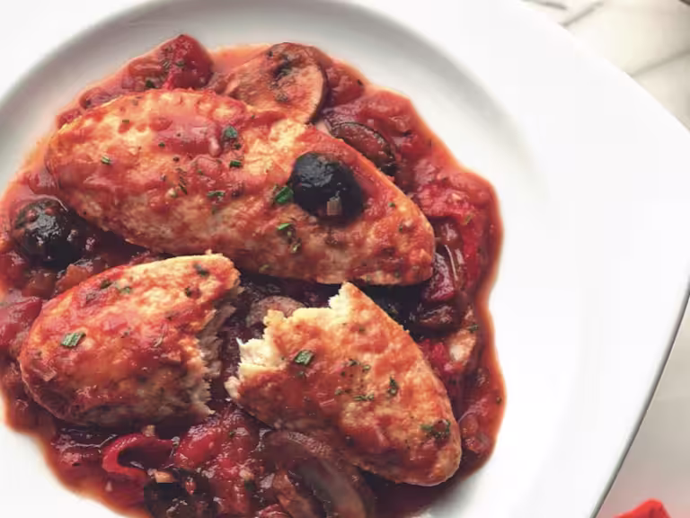 Meatless Quorn Fillets chicken cacciatore served in a dish, with one fillet half cut, garnished with olives