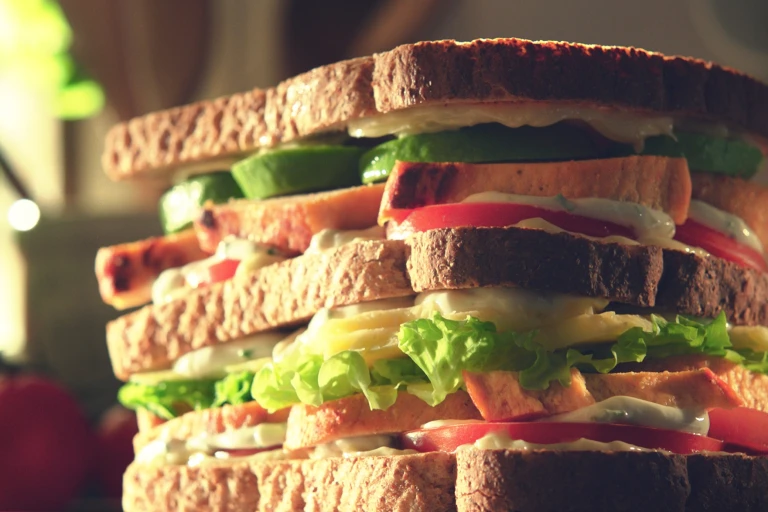 A double-decker sandwich filed with lettuce, tomatoes, avocado, Quorn Fillets, and a yogurt dressing.