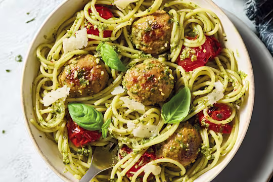 Quorn pesto pasta with spaghetti meatballs, tomatoes and parmesan with a fork in a white bowl.