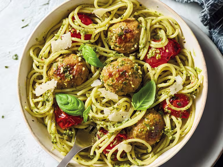 Quorn pesto pasta with spaghetti meatballs, tomatoes and parmesan with a fork in a white bowl.