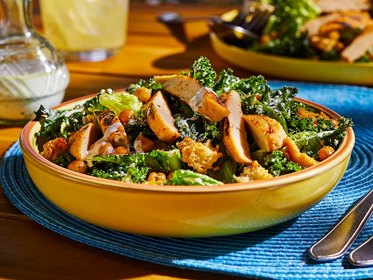Quorn Veggie Fillets with a caesar salad dressing on a bed of kale leaves in a yellow bowl.
