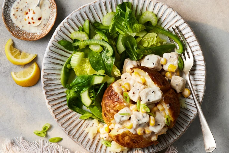 A Vegetarian Chicken and Sweetcorn Loaded Jacket Potato paired alongside a salad of spinach and green peppers.