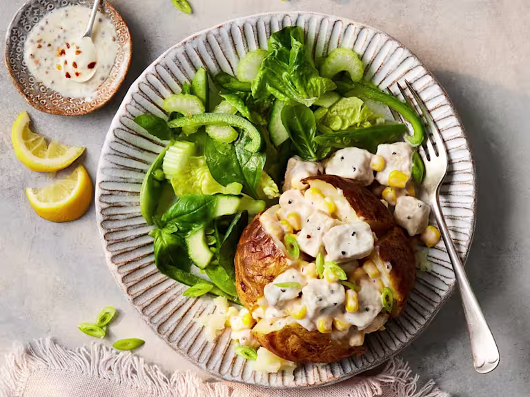 A Vegetarian Chicken and Sweetcorn Loaded Jacket Potato paired alongside a salad of spinach and green peppers.