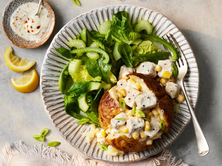 A Vegetarian Chicken and Sweetcorn Loaded Jacket Potato paired alongside a salad of spinach and green peppers.