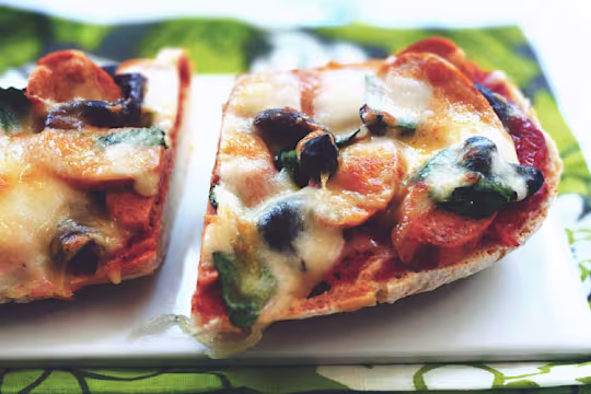 Half of a loaf of ciabatta bread topped with Quorn Sausages, bruschetta topping, black olives, and cheese.