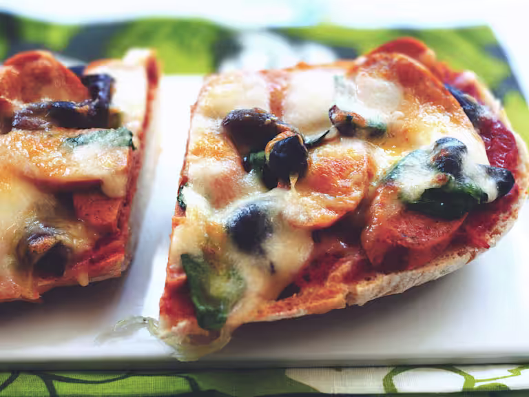 Half of a loaf of ciabatta bread topped with Quorn Sausages, bruschetta topping, black olives, and cheese.