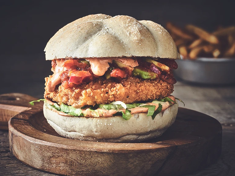 A Quorn fully loaded Cajun burger with relish in a warm bun and a bowl of French fries.