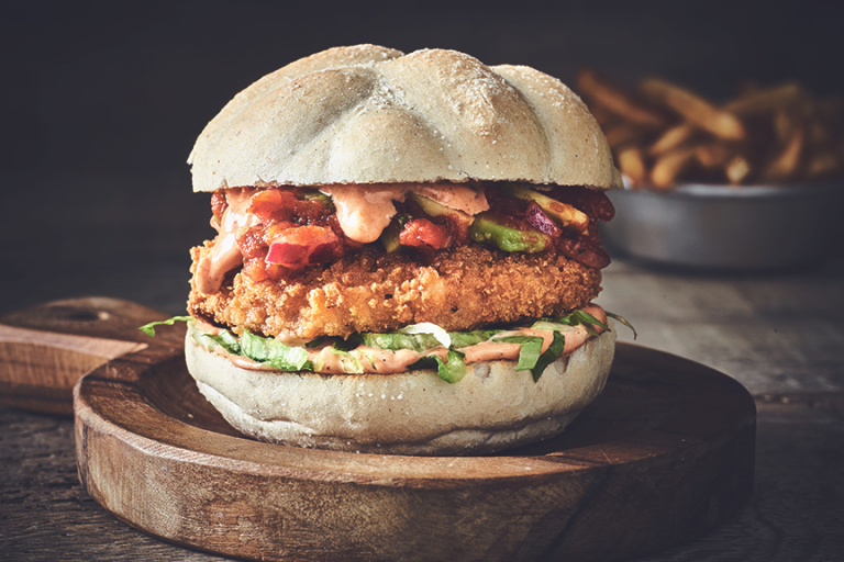 A Quorn fully loaded Cajun burger with relish in a warm bun and a bowl of French fries.