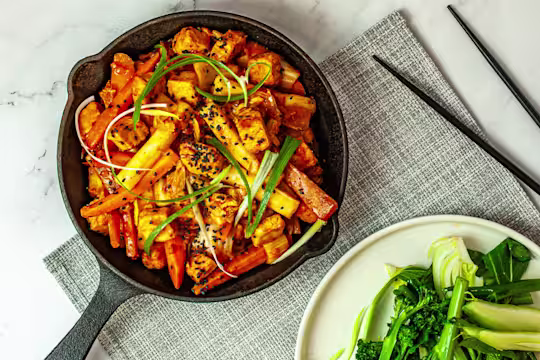 Skillet pan with Korean Dakgalbi with Quorn Vegetarian Chicken pieces served on a grey placemat with a side dish of tenderstem broccoli and black chopsticks.
