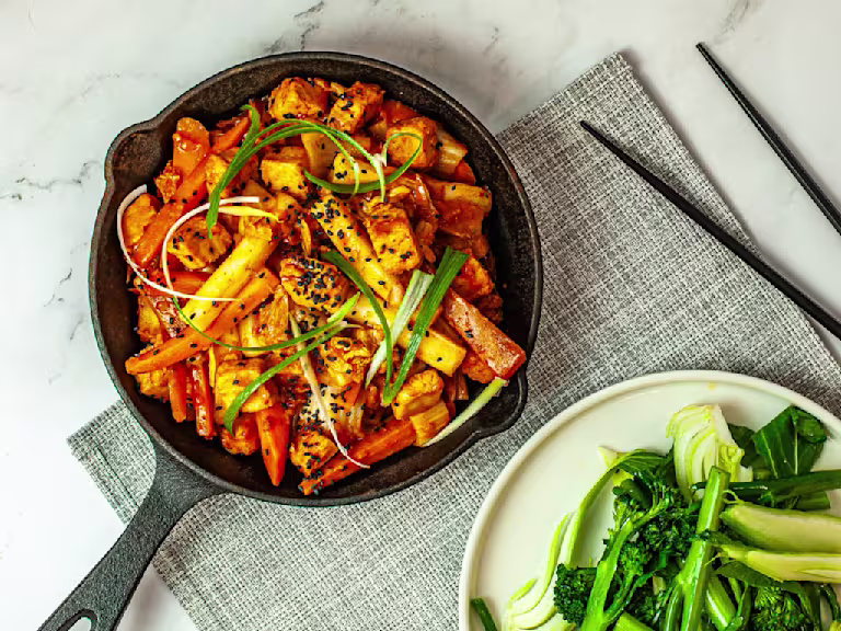 Skillet pan with Korean Dakgalbi with Quorn Vegetarian Chicken pieces served on a grey placemat with a side dish of tenderstem broccoli and black chopsticks.