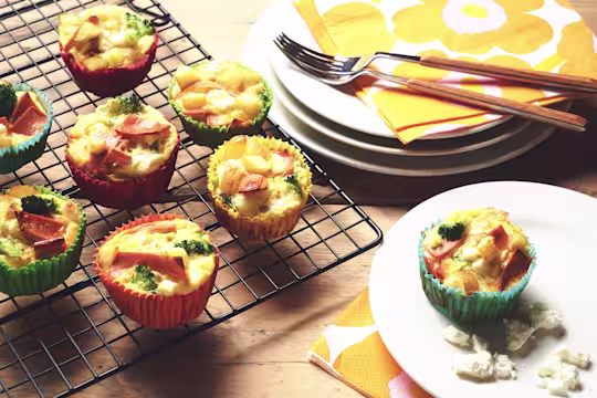 Veggie frittatas made with Quorn Vegan Ham Slices, potato and broccoli in muffin cases on a wire rack with one on a plate.