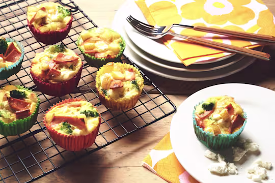 Veggie frittatas made with Quorn Vegan Ham Slices, potato and broccoli in muffin cases on a wire rack with one on a plate.
