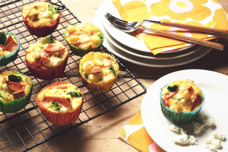 Veggie frittatas made with Quorn Vegetarian Bacon Slices, potato and broccoli in muffin cases on a wire rack with one on a plate