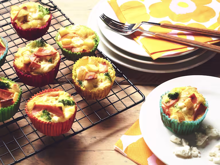 Veggie frittatas made with Quorn Vegan Ham Slices, potato and broccoli in muffin cases on a wire rack with one on a plate.
