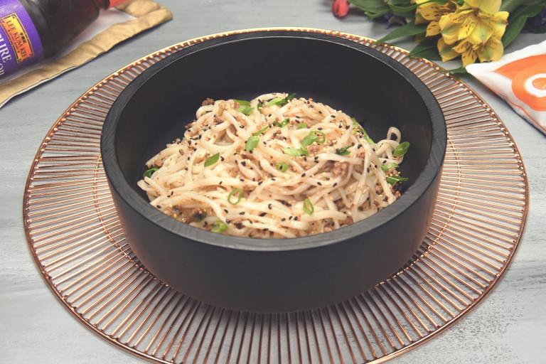 Thin noodles topped with sliced green onions, black and white sesame seeds, and Quorn Grounds in a dark bowl.