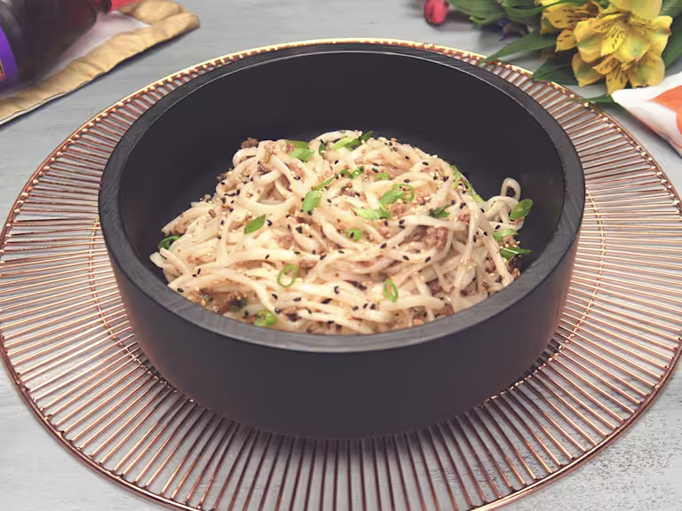 Thin noodles topped with sliced green onions, black and white sesame seeds, and Quorn Grounds in a dark bowl.