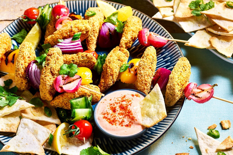 Quorn Sriracha Crumbed Tenders  arranged on skewers with fresh vegetables with pita chips and bang bang sauce on the side.