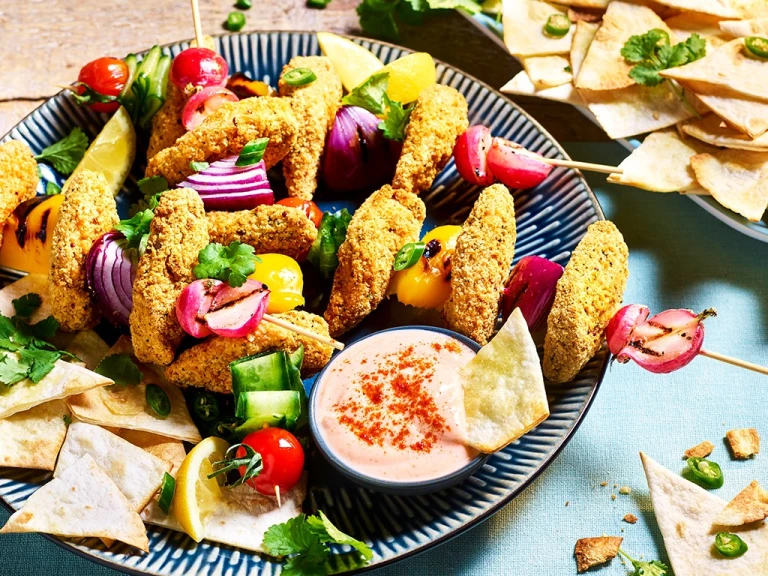 Southern Fried Bites arranged on skewers with fresh vegetables with pita chips and bang bang sauce on the side.