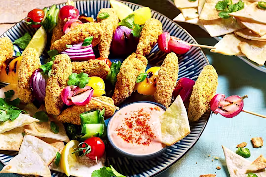 Southern Fried Bites arranged on skewers with fresh vegetables with pita chips and bang bang sauce on the side.