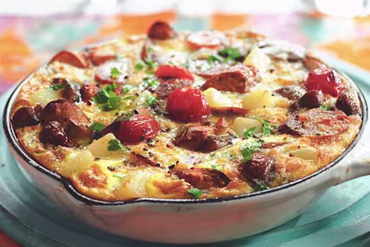 A frittata made with Quorn Sausages, tomatoes, potatoes, and mushrooms in a white cast iron skillet.