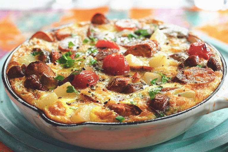 A frittata made with Quorn Sausages, tomatoes, potatoes, and mushrooms in a white cast iron skillet.