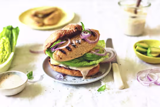 A Quorn Fillet atop cucumber, red onions, and romaine lettuce on a bun smeared with vegan Caesar dressing.