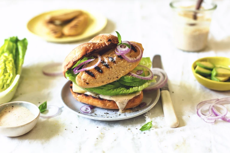 A burger bun topped with a Caesar dressing, romaine lettuce, avocado, red onion, and a charred Quorn Vegetarian Fillet.