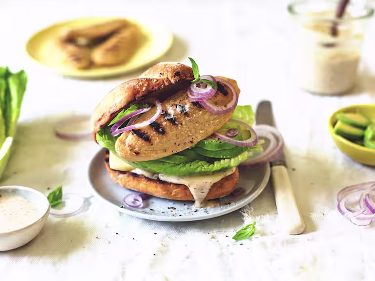 A Quorn Fillet atop cucumber, red onions, and romaine lettuce on a bun smeared with vegan Caesar dressing.