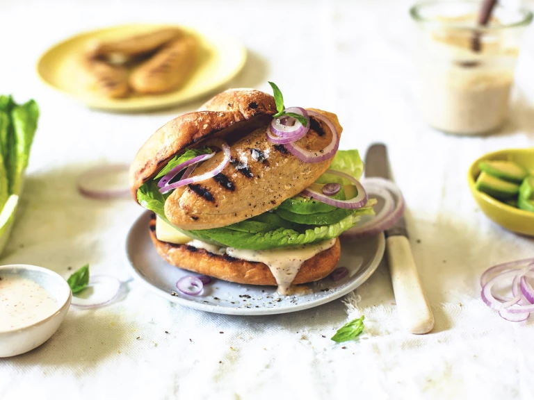 A burger bun topped with a Caesar dressing, romaine lettuce, avocado, red onion, and a charred Quorn Vegetarian Fillet.