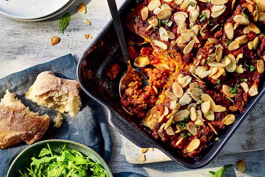 Eggplant and butternut squash lasagna with Quorn grounds served in a baking tray with ciabatta and salad leaves on the side.