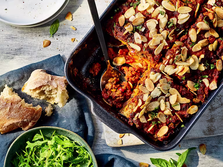Eggplant and butternut squash lasagna with Quorn grounds served in a baking tray with ciabatta and salad leaves on the side.