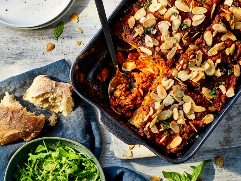 Eggplant and butternut squash lasagna with Quorn grounds served in a baking tray with ciabatta and salad leaves on the side.