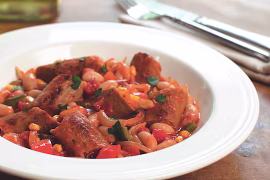 A casserole made with Quorn Sausages, beans, and sweetcorn served in a white bowl.